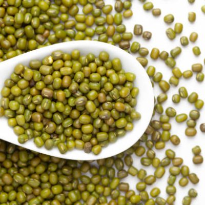 macro Close-up of Organic green Gram (Vigna radiata) or whole green moong dal on a white ceramic soup spoon. Top view, over gradient background of itself.